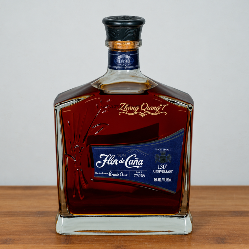 A bottle of Fór de Cava Grand Cru 130th Anniversary rum, presented in a clear glass bottle with a dark amber liquid, a blue label, and a black cap, set on a wooden surface against a neutral gray background.