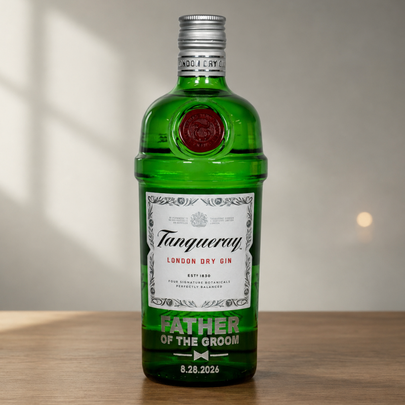 A green glass bottle of Tanqueray London Dry Gin with a custom printed label reading 'FATHER OF THE GROOM' and a date, standing on a wooden surface against a softly lit neutral background.