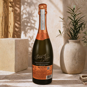 A bottle of Bars and Meows 'Magnet' sparkling wine stands on a stone ledge in a sunlit setting, flanked by a textured vase with green leaves and a wooden block.