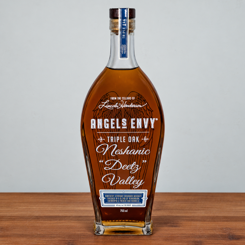 Angels Envy Triple Oak Neshanic Deutz Valley whiskey bottle on a wooden surface against a light gray background.