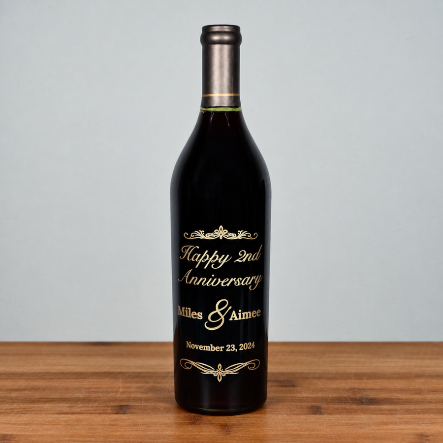 A dark glass caymus wine bottle with a metallic silver foil neck and a custom printed gold label celebrating a 2nd Anniversary, standing on a wooden surface against a light gray background.