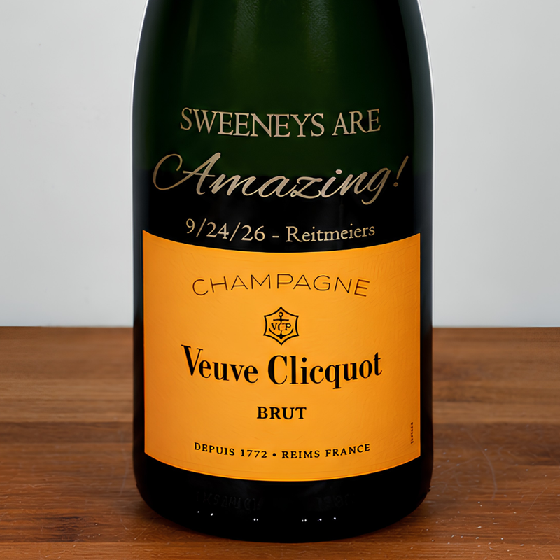 A bottle of Veuve Clicquot Brut champagne with a custom printed label that reads 'SWEENEYS ARE Amazing! 9/24/26 - Reitmeiers' in gold lettering on a dark green bottle with a bright orange label.