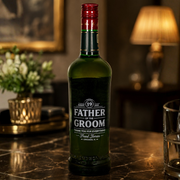 A green glass bottle of Father of the Groom alcohol-free spirit by Fred Jones, styled on a dark marble bar counter with a warm, dimly lit background featuring a lamp and flowers.