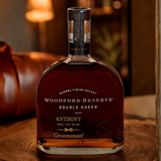 A bottle of Woodford Reserve Double Oaked bourbon whiskey with a custom printed label reading 'Anthony Will You Be My Groomsman?' in a warm, rustic indoor setting.