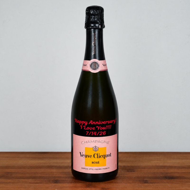 A bottle of Veuve Clicquot Rosé champagne with a custom pink anniversary label reading 'Happy Anniversary I Love You!!! 7/19/26' on a wooden surface against a plain light gray background.