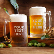 Two glasses of beer with 'Your Text Here' text, surrounded by hops and a wooden barrel on a wooden surface.