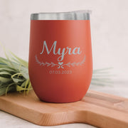 Red orange insulated tumbler with 'Myra' and a date on a wooden surface