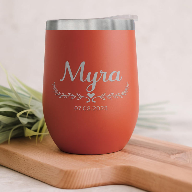Red orange insulated tumbler with 'Myra' and a date on a wooden surface