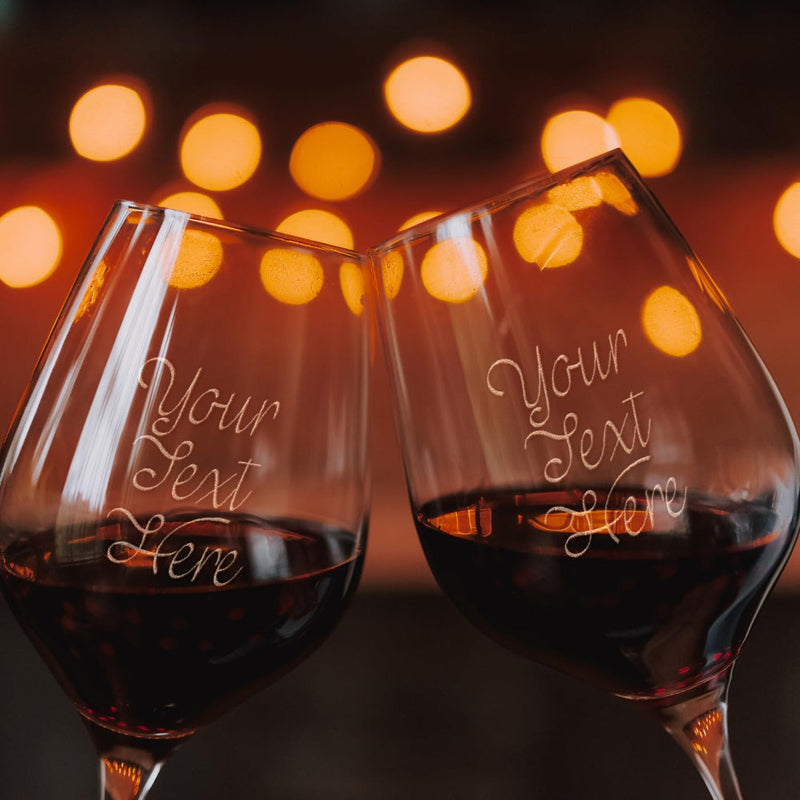 Two wine glasses with personalized text against a blurred lights background