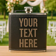 Personalized black leather flask with 'YOUR TEXT HERE' on a blurred outdoor background
