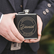 Person holding a black flask with engraved text, wearing a suit.