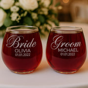 Two stemless wine glasses filled with red liquid, personalized for 'Bride Olivia' and 'Groom Michael', with a blurred floral background.