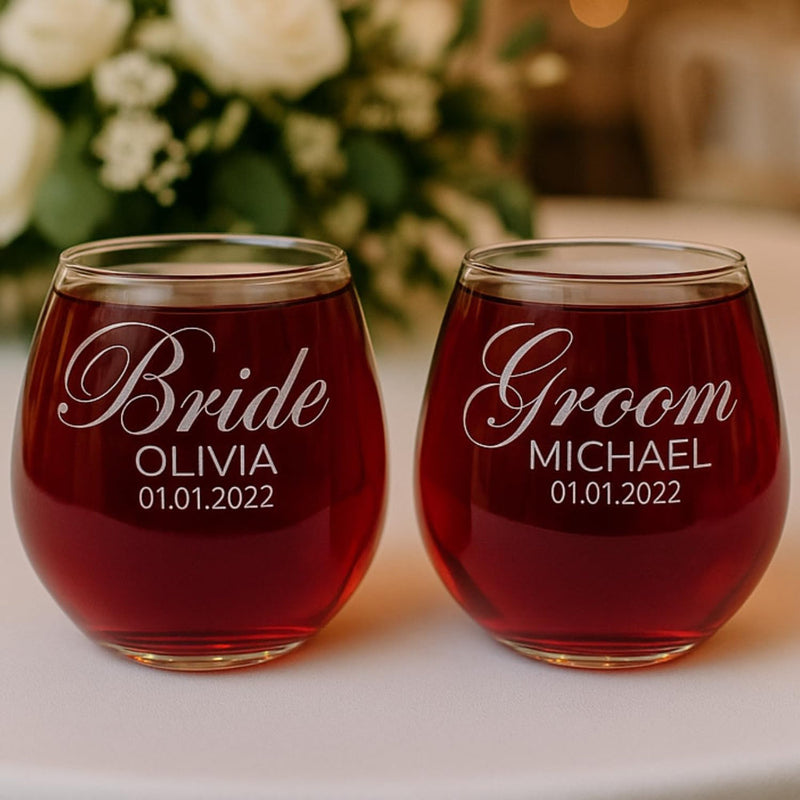 Two stemless wine glasses filled with red liquid, personalized for 'Bride Olivia' and 'Groom Michael', with a blurred floral background.