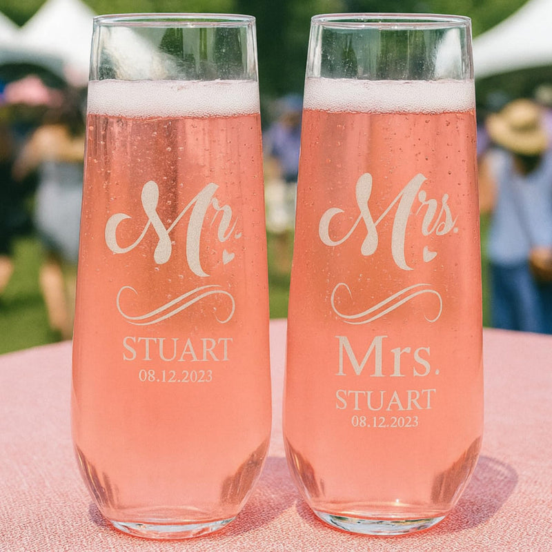 Two champagne flutes with 'Mr. Stuart' and 'Mrs. Stuart' engraving on a pink surface.