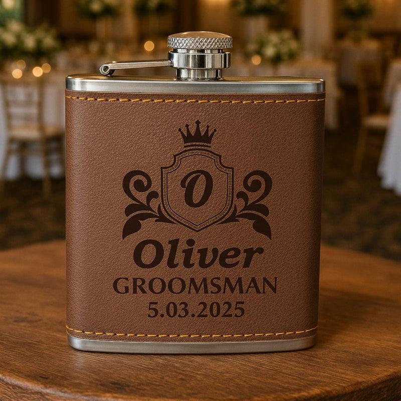 Brown leather flask with engraved text on a wooden surface, blurred background of a wedding reception.