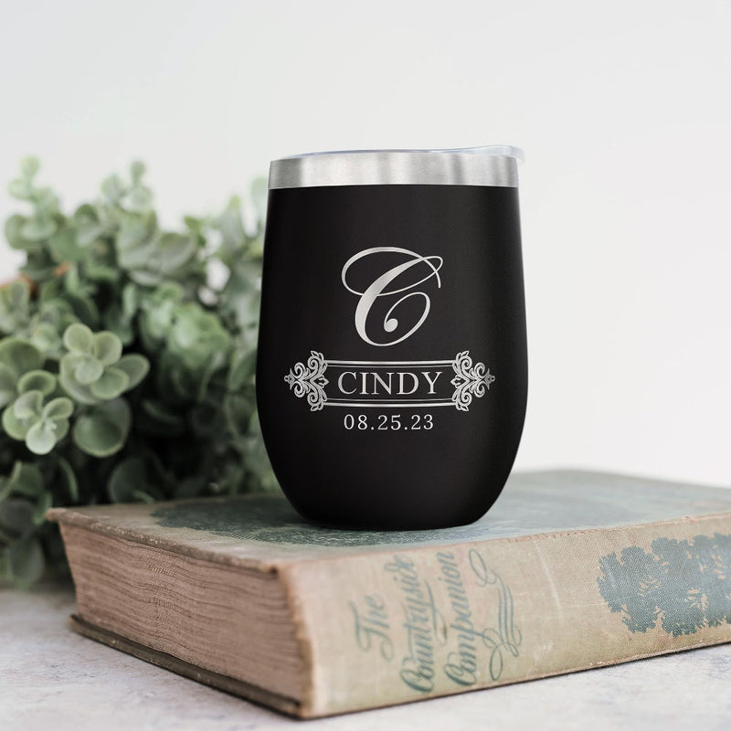 Black tumbler with silver lid on a book with greenery in the background