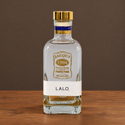 A clear glass bottle of Lalo. spirit with a gold cap, a white label reading 'LALO.