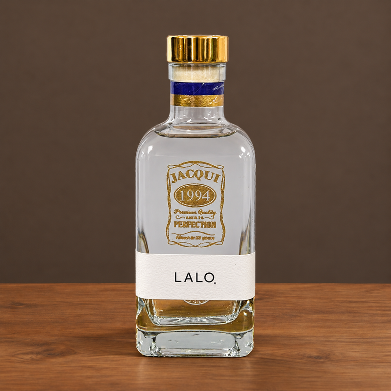 A clear glass bottle of Lalo. spirit with a gold cap, a white label reading 'LALO.