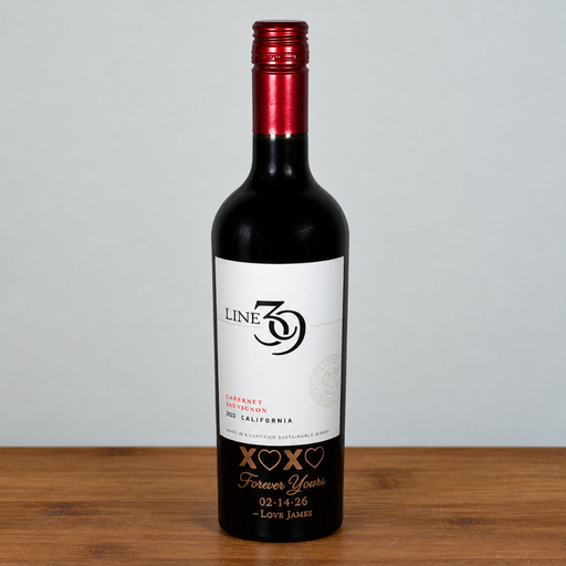 A custom line 39 red wine bottle with a red foil neck cap and a white personalized label, standing on a wooden surface against a light gray background.